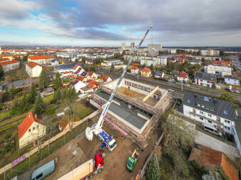 Ein großer Dachbalken wird auf ein Gebäude gehoben. Blick aus der Vogelperspektive.