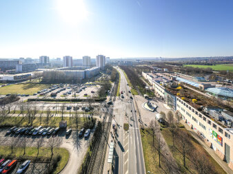 Luftaufnahme einer mehrspurigen Straße, rechts ein langgezogenes Gebäude mit Einkaufszentrum