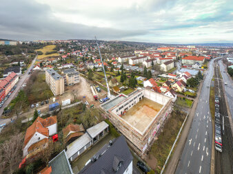 Ein großer Dachbalken wird auf ein Gebäude gehoben. Blick aus der Vogelperspektive.