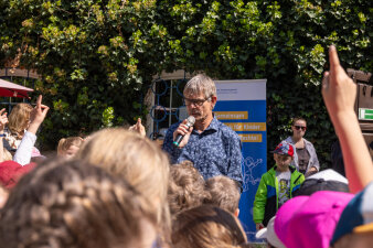Ein Mann spricht vor vielen Kindern in ein Mikrofon.