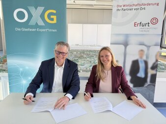 ein Mann und eine Frau sitzen an einem Tisch und unterschreiben jeweils ein vertragsartiges Papier