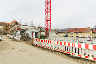 Um den Rohbau einer Schule steht ein Gerüst. Das Gelände ist mit Warnbaken abgesperrt.