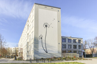 Ein saniertes Schulgebäude. Auf der Fassade ist eine Pusteblume zu sehen.