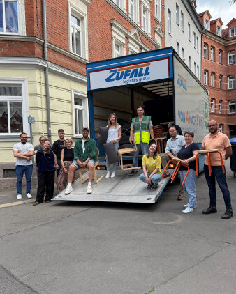 zwölf Personen stehen an und auf der Rampe eines mit Möbeln befüllten LKW