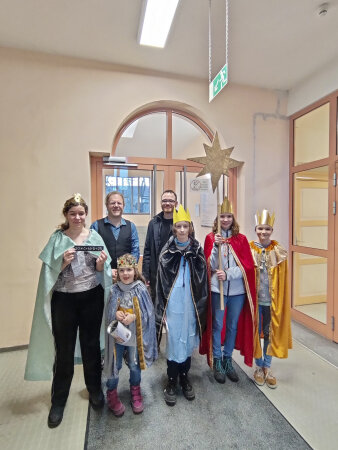 fünf Sternsinger-Kinder mit Umhang und Kronen stehen vor zwei erwachsenen Männern