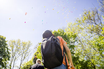 Ein Kind blickt vielen bunten Luftballons am Himmel hinterher.