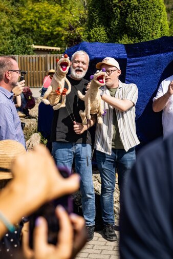 zwei Handpuppenspieler mit Stoffiguren vor mit Stoff verhüllter Plastik