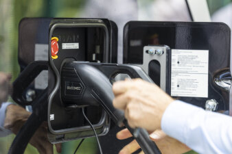 eine schwarze Elektroladestation, eine Person hat den Hand am Laderüssel