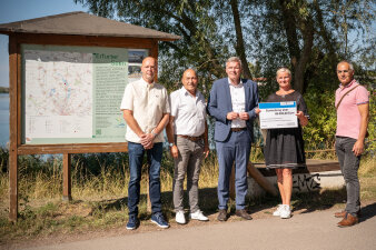 fünf Personen vor einer Informationstafel an einem See