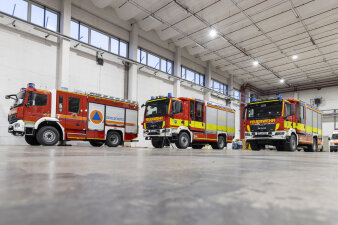 Drei neue Feuerwehrfahrzeuge stehen in einer großen Halle.