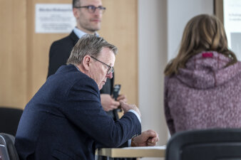 ein Mann mit Brille sitzt an einem Tisch und spricht in die Runde