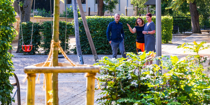drei Personen stehen auf einem Spielplatz in einer Parkanlage