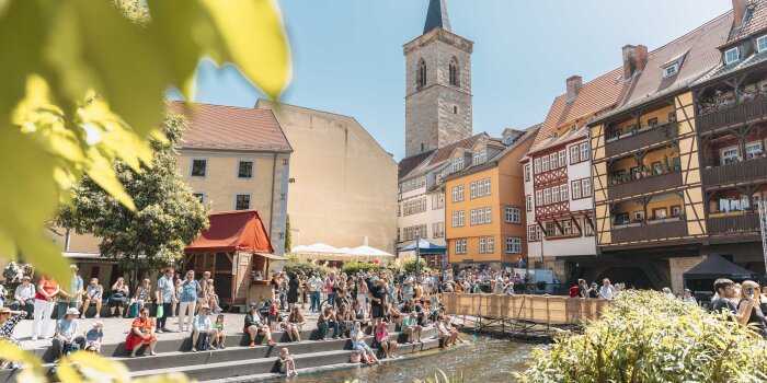 eine bebaute Brücke, davor viele Menschen und einige Zelte