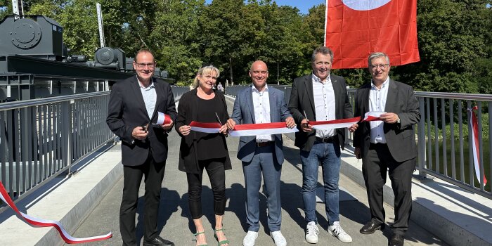 Fünf Personen stehen auf einer Brücke und haben ein gespanntes Band durchschnitten