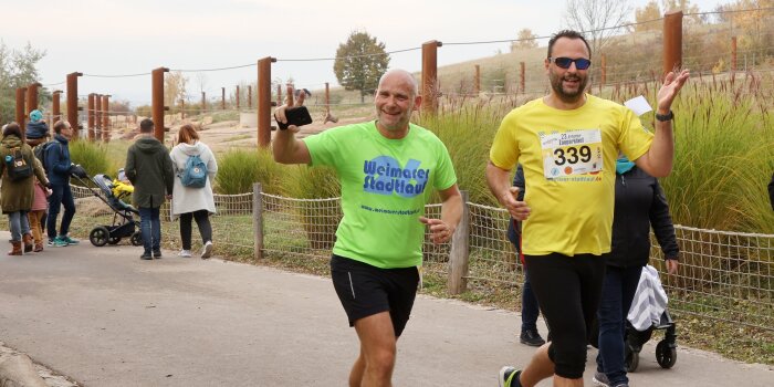 Foto: Zooparklauf © Karina Hessland-Wissel Zwei Personen in Laufkleidung joggen an einem Tiergehege vorbei, im Hintergrund Zuschauer