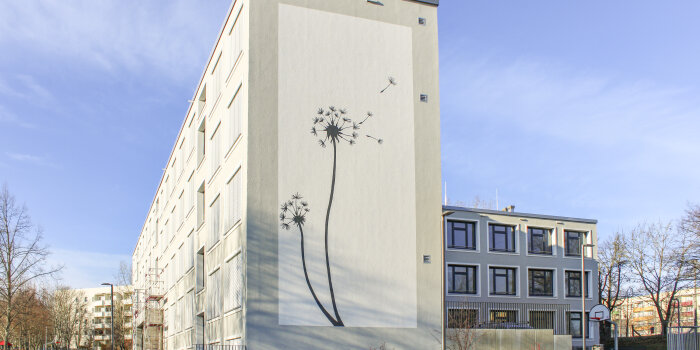 Ein saniertes Schulgebäude. Auf der Fassade ist eine Pusteblume zu sehen.