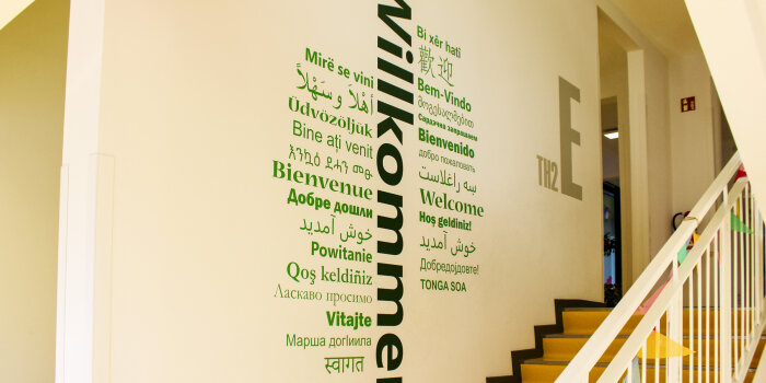 Das Wort „Willkommen“ steht in vielen Sprachen an der Wand eines Treppenaufgangs. 