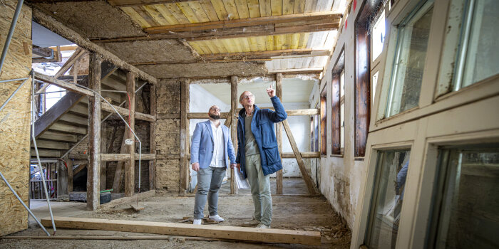 Zwei Männer auf einer Baustelle in einem Haus mit freigelegten Balken und Mauerwerk