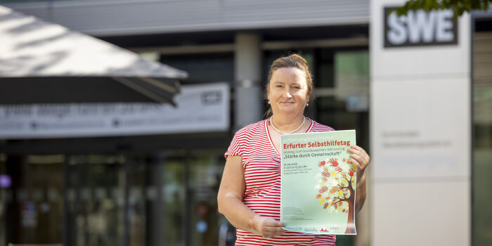 Eine Frau trägt ein rot-weiß gestreiftes Shirt und hält ein grünes Plakat in der Hand. 