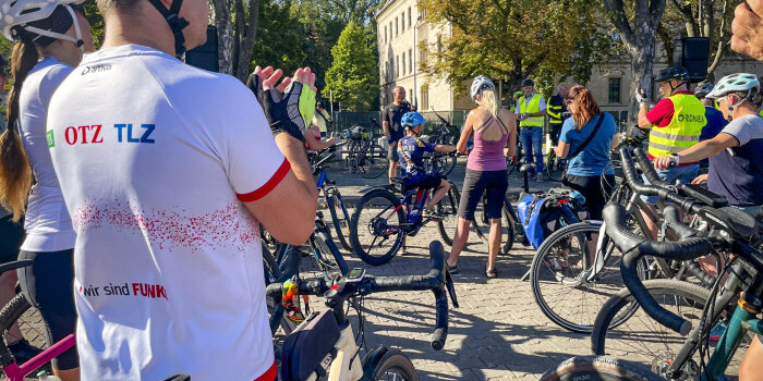 zahlreiche Radfahrer stehen auf einem städtischen Platz; ein Mann spricht in ein Mikrofon