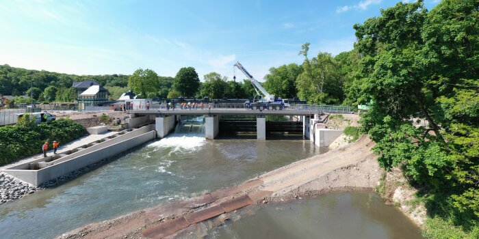 Ein Wehr über einem Fluss, darauf steht ein Kran, Eine Schleuse ist geöffnet, aus ihr strömt Wasser. 