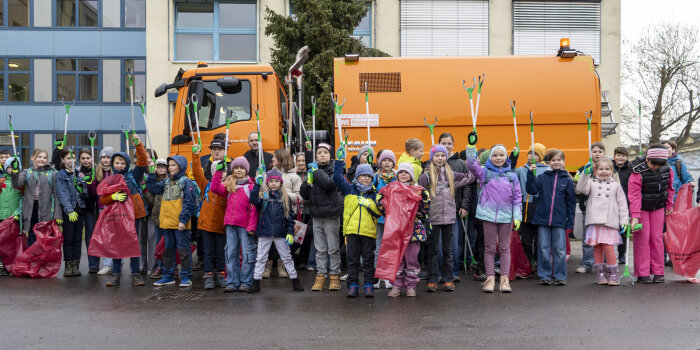 viele Kinder stehen in einer Reihe vor einem Müllfahrzeug, in der Hand halten sie Müllsäcke und Greifer