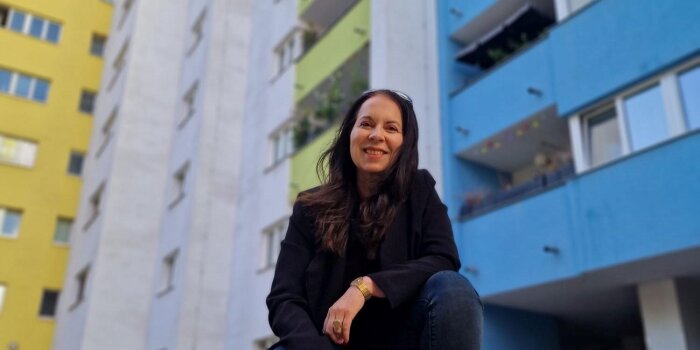 Foto: Isabella Straub (Stadtschreiberin 2023) © Susanne Kriste eine Frau posiert in der Hocke vor Hochhäusern