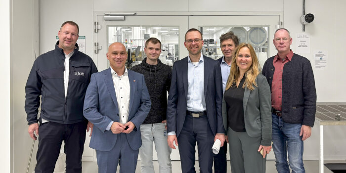 sechs Personen stehen vor einer Glastür, durch die Produktions- oder Laborräume zu sehen sind