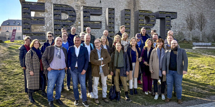 Eine Gruppe von 29 Menschen steht vor einem Schriftzug. Dieser zeigt das Wort: Erfurt. 