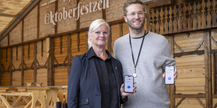zwei Personen halten ein Handy, auf dem Display ist der Schriftzug "Drücken um Helfer alarmieren"