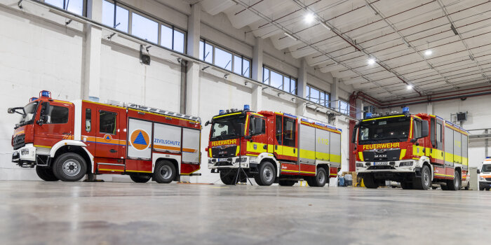 Drei neue Feuerwehrfahrzeuge stehen in einer großen Halle.