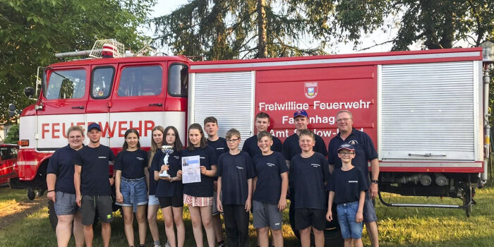 Elf Jugendliche und drei Erwachsene stehen vor einem Feuerwehrauto. Eine Jugendliche hält eine Urkunde in der Hand.