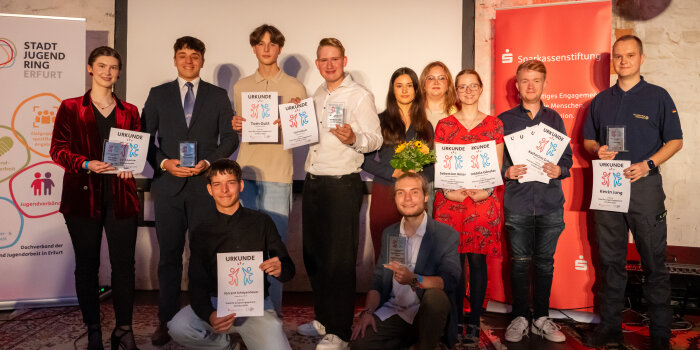 Eine Gruppe von Personen steht mit Urkunden in der Hand vor einer Leinwamd