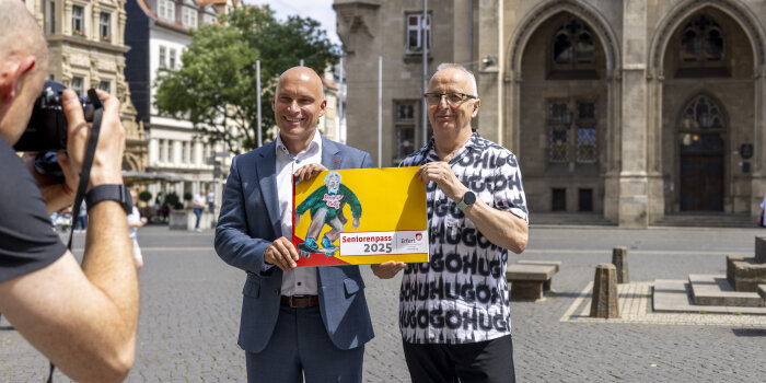 Foto: Präsentation des Seniorenpasses © Stadtverwaltung Erfurt Zwei Männer stehen auf einem Platz und halten ein großes Buch in den Händen mit der Aufschrift Seniorenpass 2025