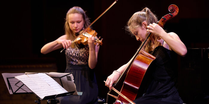 zwei festliche gekleidete Mädchen, eins spielt Geige, eins Violoncello
