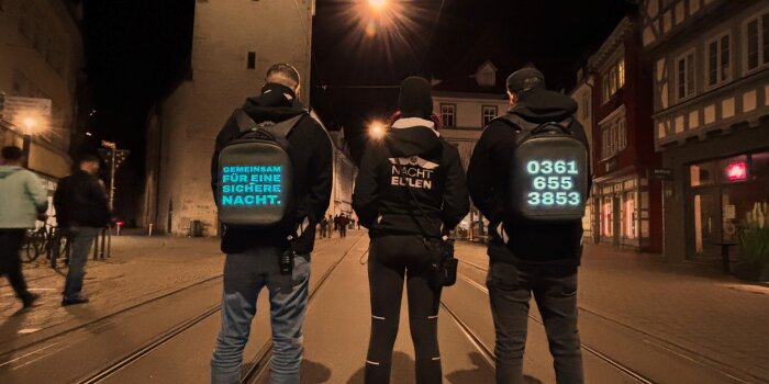 Foto: Erfurter Nachteulen © Stadtverwaltung Erfurt Drei Personen mit leuchtenden Rucksäcken in einer dunklen Straße
