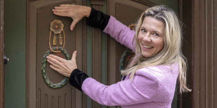 eine Frau mit blonden Haaren hält die Hände um ein verziertes Detail einer Eingangstür
