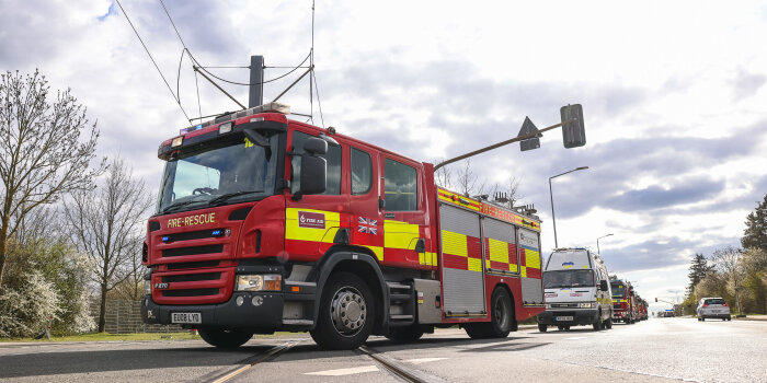 Mehrere Feuerwehrfahrzeuge fahren in Kolonne eine Straße entlang. 