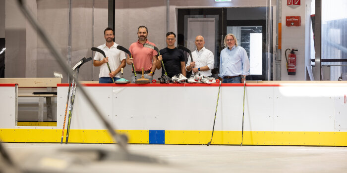 Fünf Männer mit Eishockeyschlägern hinter einer Bande