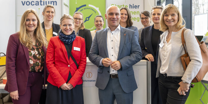 neun Frauen und ein Mann stehen an einem Messestand