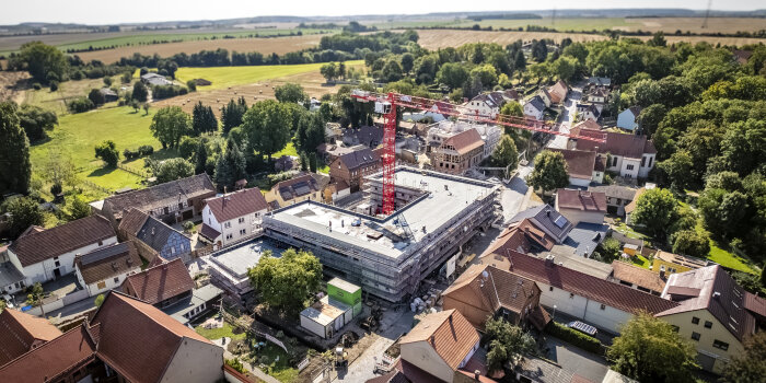 Luftaufnahme einer Baustelle inmitten von Häusern. Zentral steht ein großer, roter Kran. 