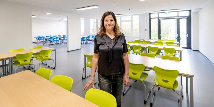 Eine Frau steht in einem Raum mit Tischen und bünten Stühlen