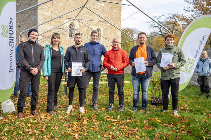 sieben Personen stehen in einer Reihe, drei halten eine Auszeichnung in der Hand