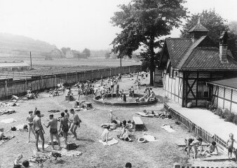 Menschen stehen in Badekleidung auf einer Wiese, in der Mitte ein Planschbecken