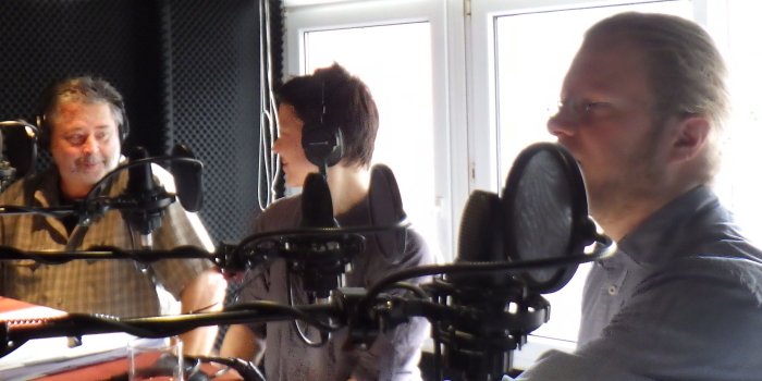 drei Personen in einem Radio-Studio hinter Mikrofonen