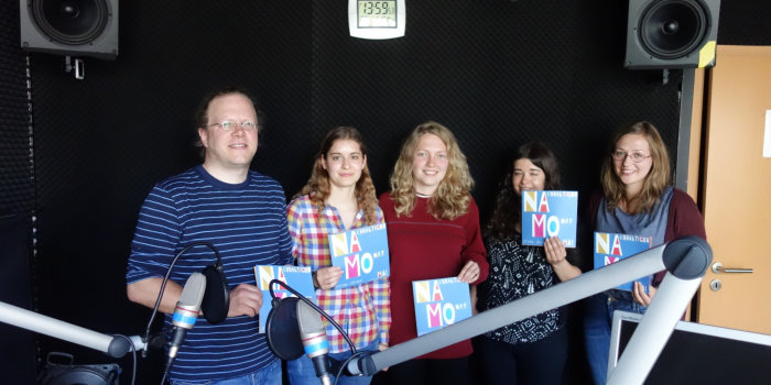 vier Frauen und ein Mann im Studio stehend und den Flyer "NaMo" haltend
