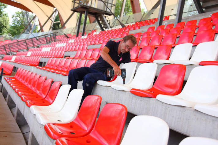 Ein Arbeiter schraubt einen weißen Sitz auf der Tribüne fest.