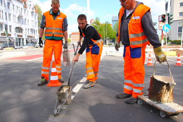 drei Arbeiter beim Aufbringen von Straßenmarkierungen