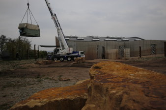 Ein Container auf einem LKW vor der Elefantenanlage wird mit einem Kran, der auf der Anlage steht, angehoben.