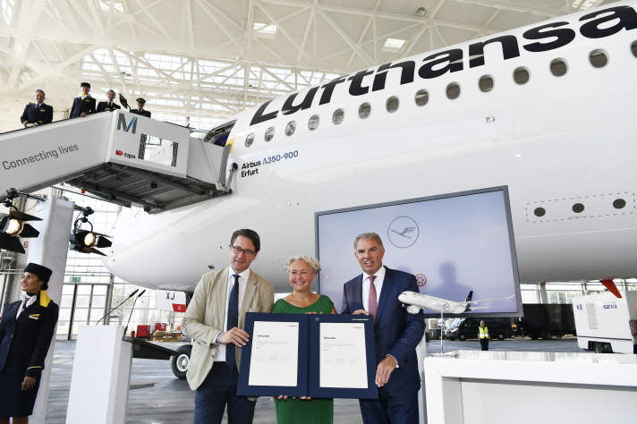 Frau und zwei Männer posieren mit Urkunde vor Flugzeug